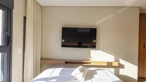 Habitació d'hotel amb un llit, un televisor de pantalla plana al mur i una finestra amb cortines.