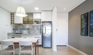 Eine moderne Küche mit weißen Schränken, einem Edelstahlkühlschrank und einem Essbereich mit weißem Tisch und Stühlen.