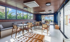 Ein modernes Interieur mit Holzboden, großen Fenstern und einer Sitzecke mit Tischen und Stühlen.