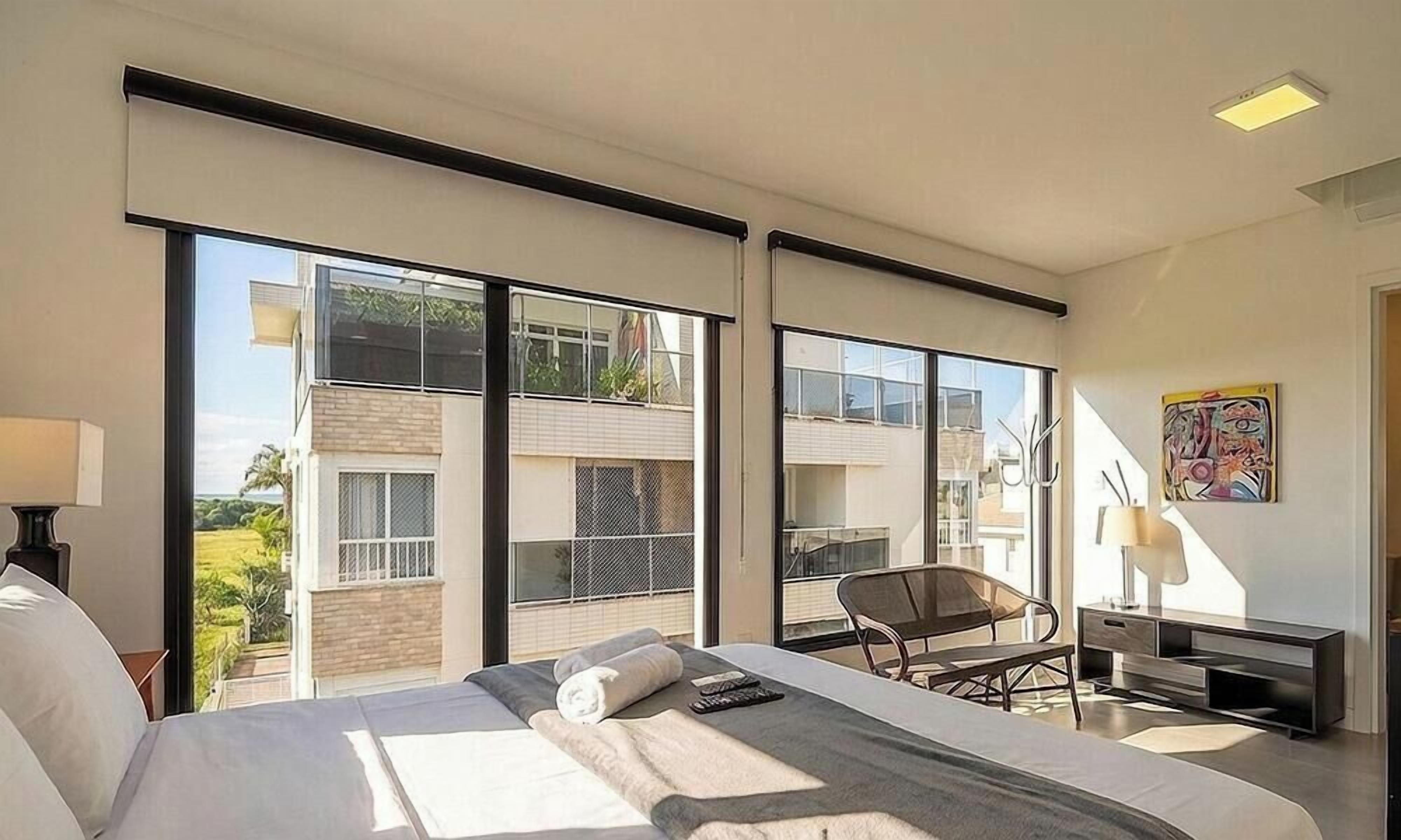 Quarto de hotel moderno com uma cama grande, uma cadeira, uma escrivaninha e vista para o exterior.