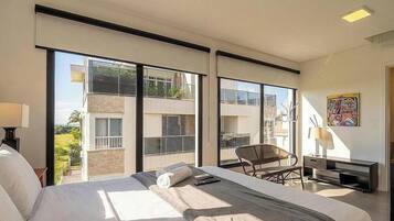 Quarto de hotel moderno com uma cama grande, uma cadeira, uma escrivaninha e vista para o exterior.
