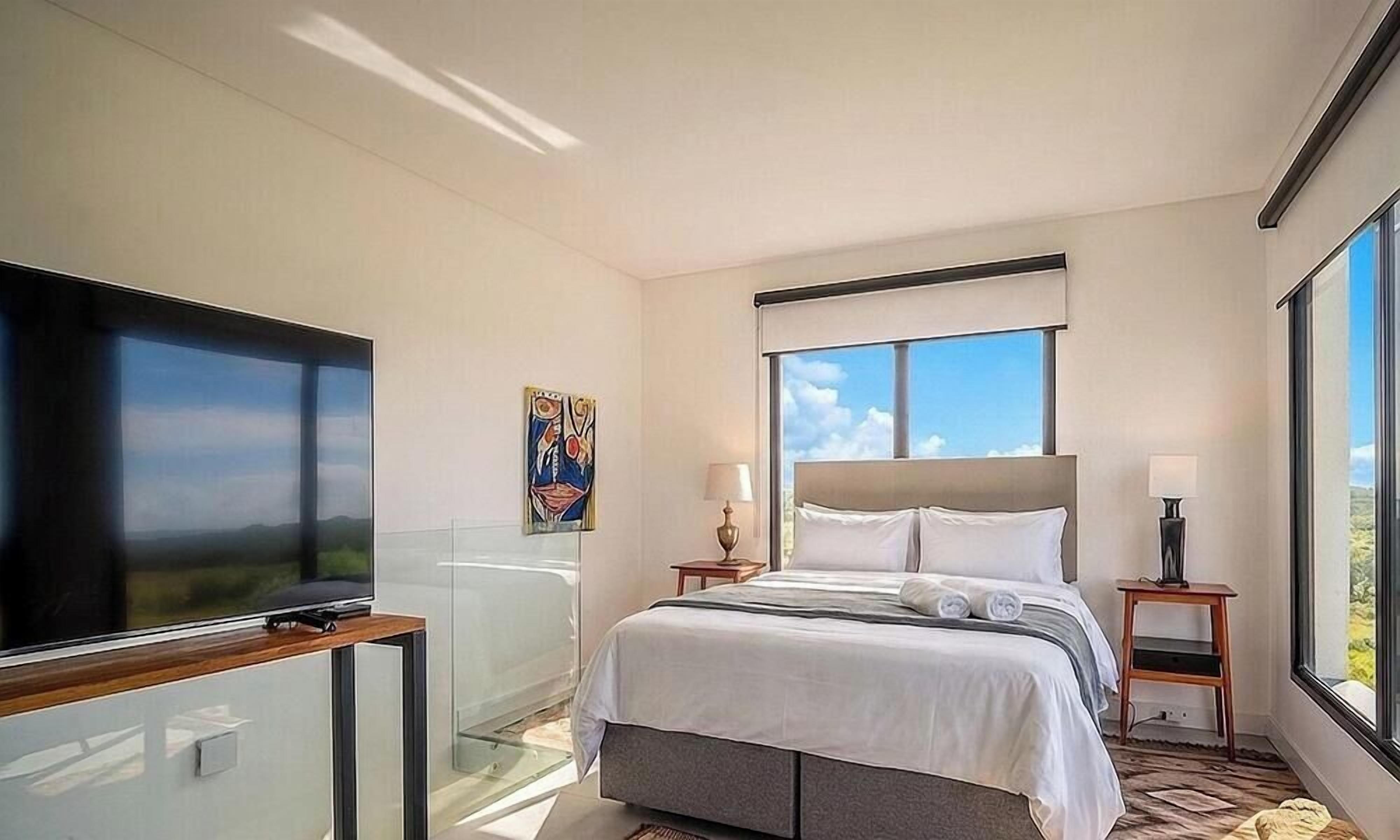 Quarto de hotel com cama, televisão, janela e um quadro na parede.