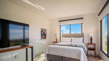 Quarto de hotel com cama, televisão, janela e um quadro na parede.