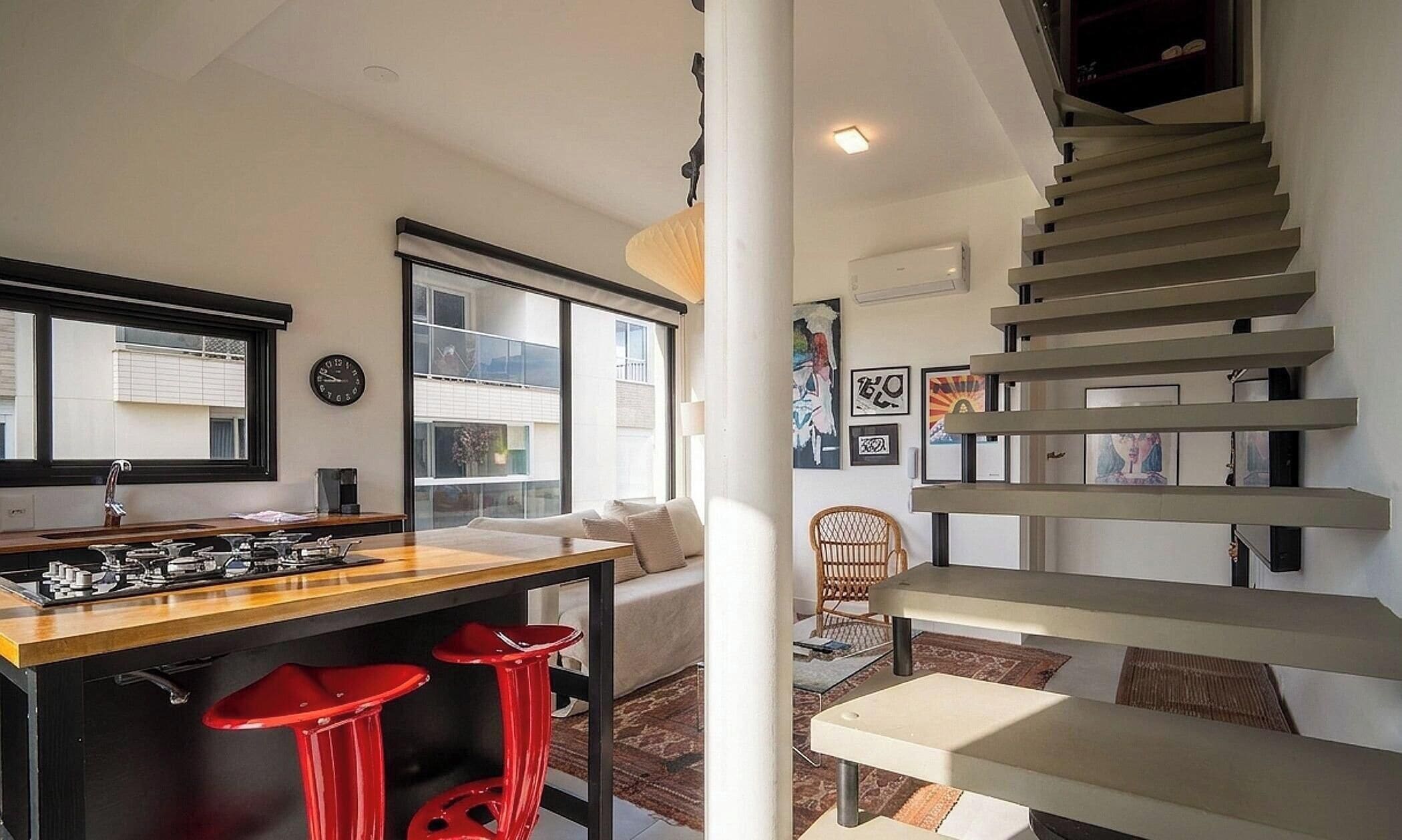 A modern kitchen with a gas stove, red bar stools, and a large window.