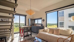 Ein modernes Interieur mit Sofa, Esstisch und Küchenbereich, mit großen Fenstern und einer Treppe.
