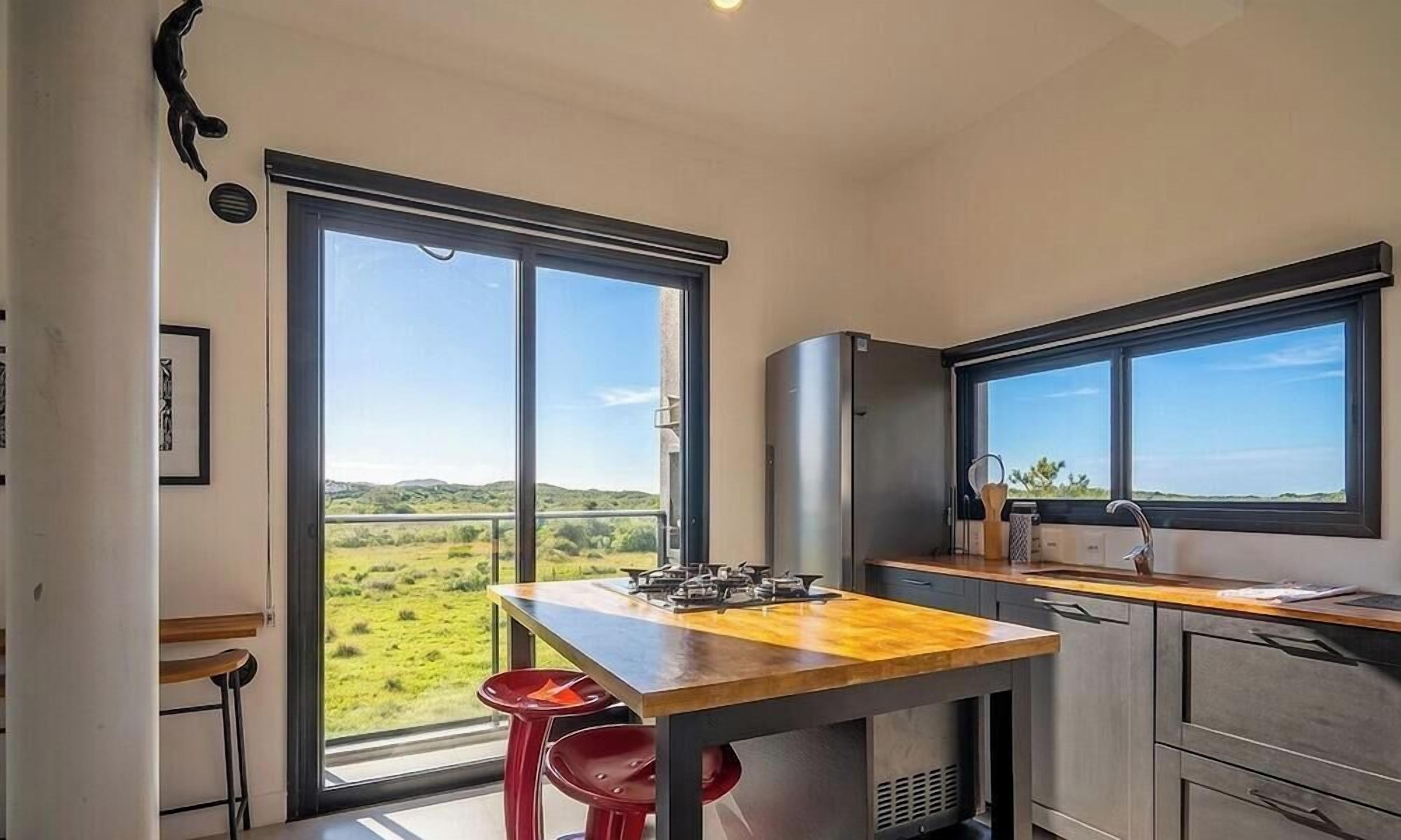Uma cozinha moderna com uma janela grande, um fogão a gás e vista para uma paisagem verde.