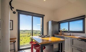 Uma cozinha moderna com uma janela grande, um fogão a gás e vista para uma paisagem verde.