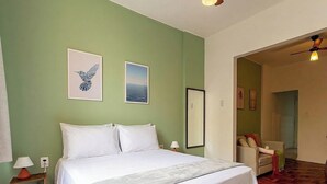 Una camera d'albergo con un letto, due quadri appesi al muro, un comodino con una lampada e una sedia nell'angolo.