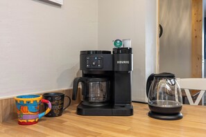 Eine Kaffeemaschine, eine Tasse und eine Karaffe auf einem Holztisch.