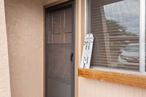Une porte surmontée d’une fenêtre, une boîte aux lettres en bois et une pancarte indiquant « Bienvenue ».