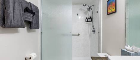 A bathroom with a glass shower enclosure, a toilet, a sink, and a towel rack.