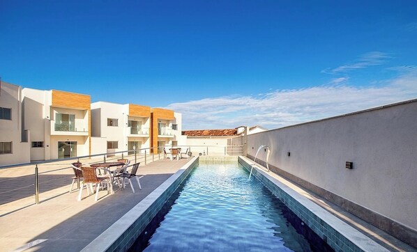 A swimming pool with a clear blue sky above, surrounded by modern buildings with balconies. - Condo Apt w/ Pool and Sea View Alm0009 (Porto Seguro)