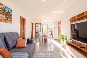 A modern living room with a sofa, TV, and dining area. - Condo Apt w/ Pool and Sea View Alm0009 (Porto Seguro)