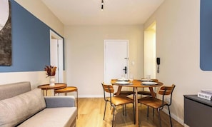 Un saló modern amb un sofà, una taula de dinar amb cadires i una taula auxiliar petita amb un ram.