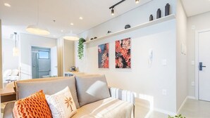 A modern living room with a sofa, decorative pillows, wall art, and a plant. - Studio in Condo w/ Pool Downtown Itapema Ffs0606 (Itapema)