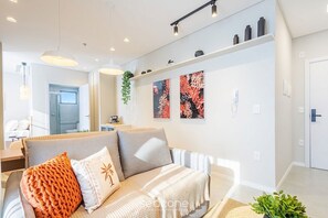 Ein stilvolles Wohnzimmer mit einer Couch, Zierkissen, Wandbild und einer Pflanze.