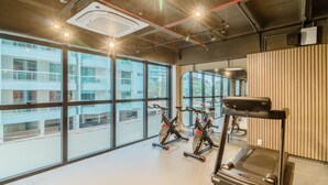 A gym with exercise equipment, large windows, and a view of a building. - Studio in Condo w/ Pool Downtown Itapema Ffs0606 (Itapema)