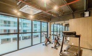 Ein Fitnessstudio mit Trainingsgeräten, großen Fenstern und Blick auf ein Gebäude.