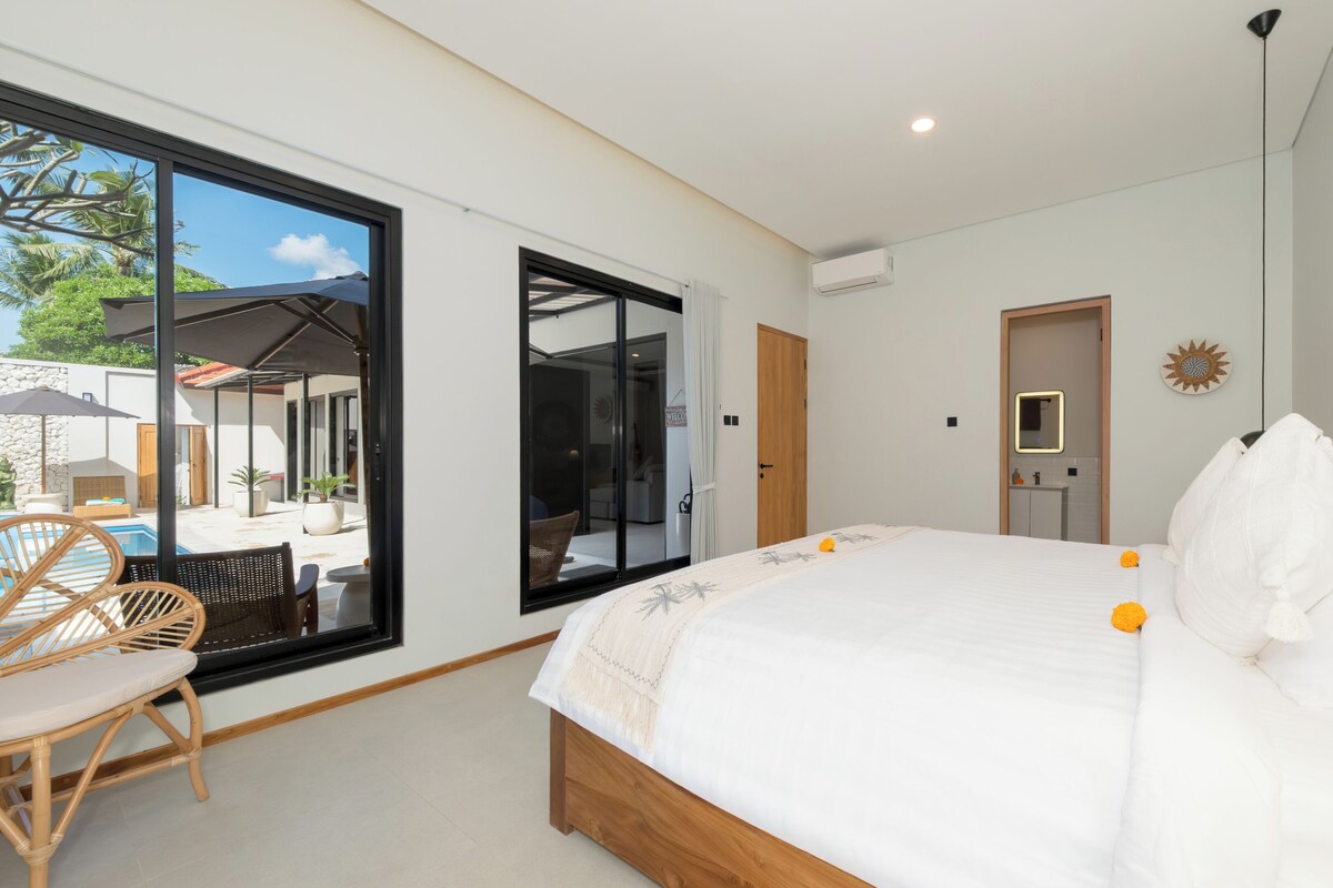 Ein modernes Schlafzimmer mit einem großen Bett, Blick ins Freie und einem Badezimmer mit Spiegel und Waschbecken.