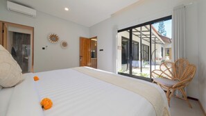 Ein Schlafzimmer mit einem großen Bett, einem Korbstuhl und Blick ins Freie.