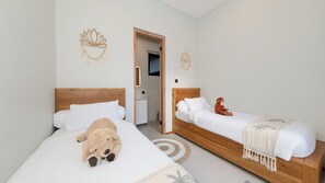 Ein Hotelzimmer mit zwei Betten, einem hölzernen Kopfteil, einem Teddybären auf dem einen Bett und einer Stoffaffe auf dem anderen.
