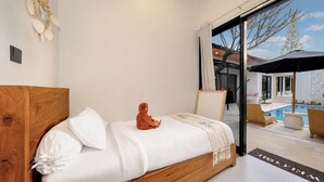 A bedroom with a wooden bed, a plush toy, and a view of an outdoor swimming pool area.