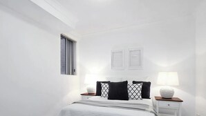A bedroom with a bed, two bedside tables, a window, and wall-mounted picture frames. - Apartment in Manly, Walk to beach (Manly)