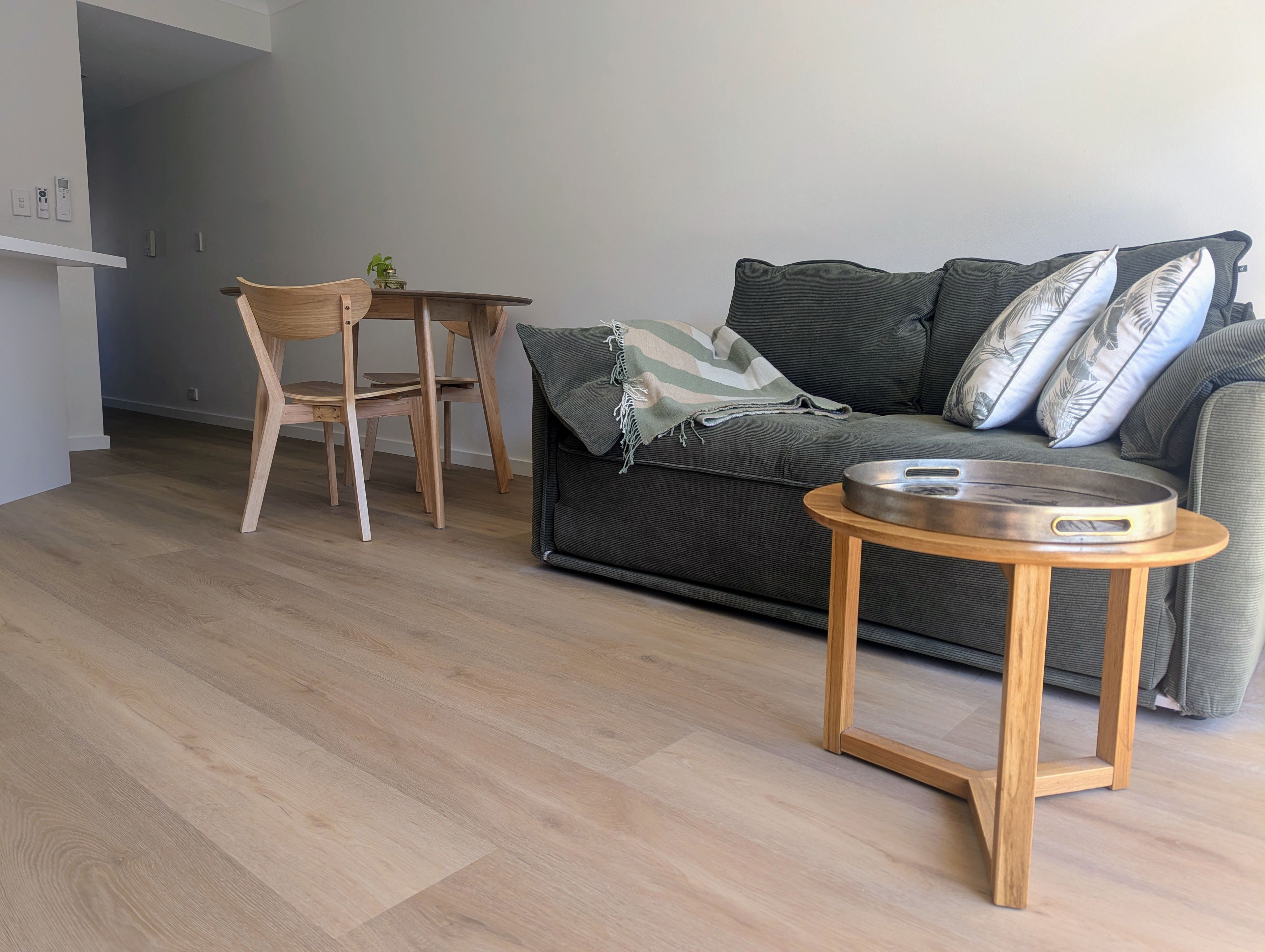A modern living room with a wooden floor, a grey sofa with patterned cushions, a small wooden table, and a chair.