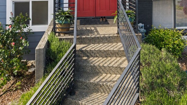 Ein zweistöckiges Haus mit roter Tür, einer kleinen Veranda und einer Treppe zum Eingang.