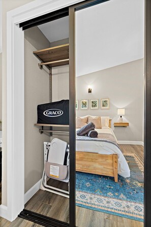 A bedroom with a bed, a nightstand, a lamp, a wall-mounted shelf with a black bag, and a window with a view. - Modern Family Retreat Near Sea-tac, Marina & Seattle (Des Moines)