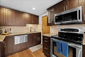A kitchen with wooden cabinets, a stainless steel microwave, and a black stove. - Modern Family Retreat Near Sea-tac, Marina & Seattle (Des Moines)