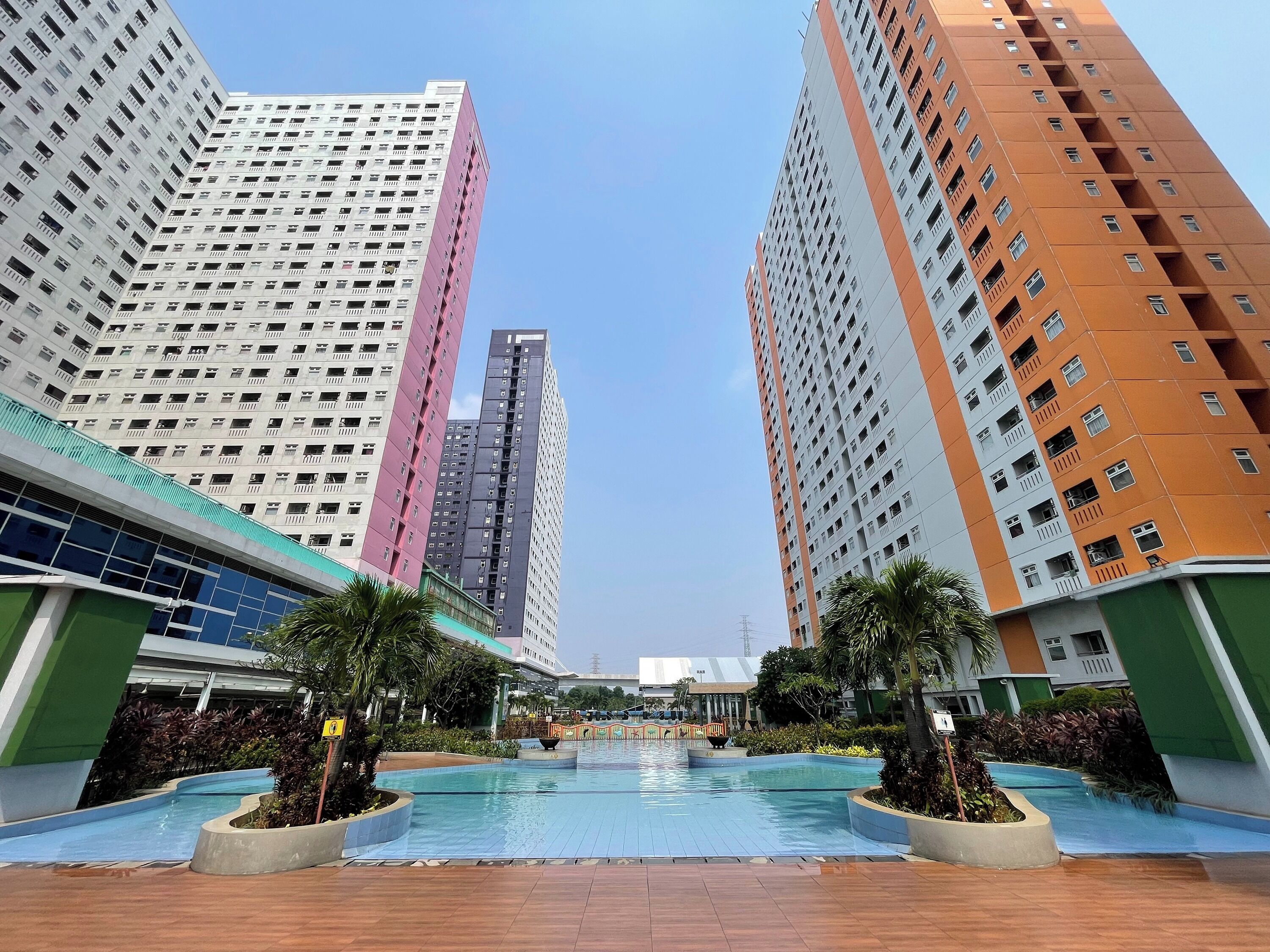 A modern building complex with multiple high-rise structures, a central swimming pool, and surrounding greenery.
