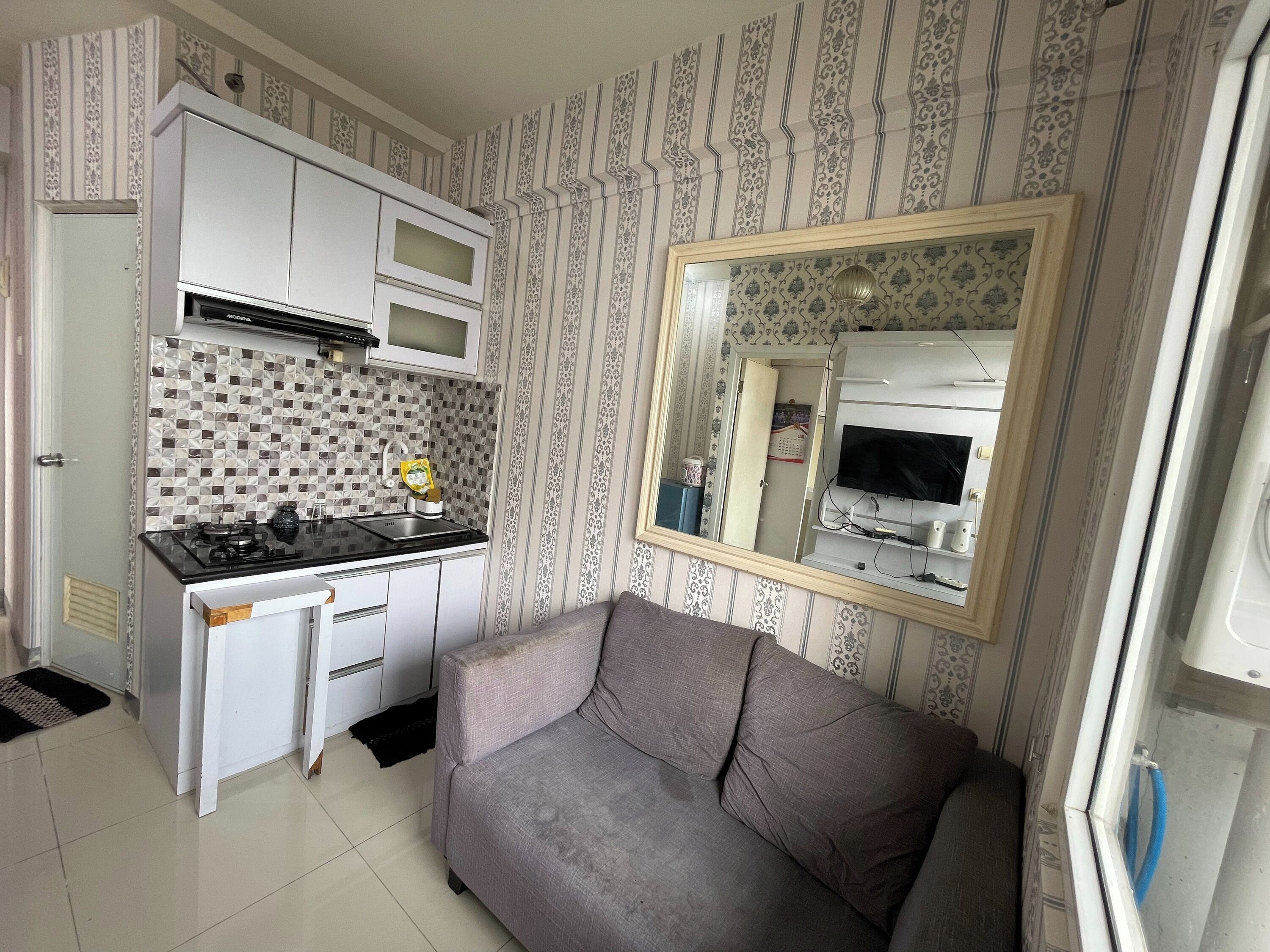 Een knus woongedeelte met een kitchenette, een bank en een grote spiegel die de ruimte weerspiegelt.