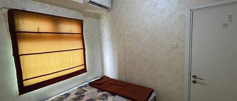 A bedroom with a bed, a window with blinds, an air conditioning unit, and a door.