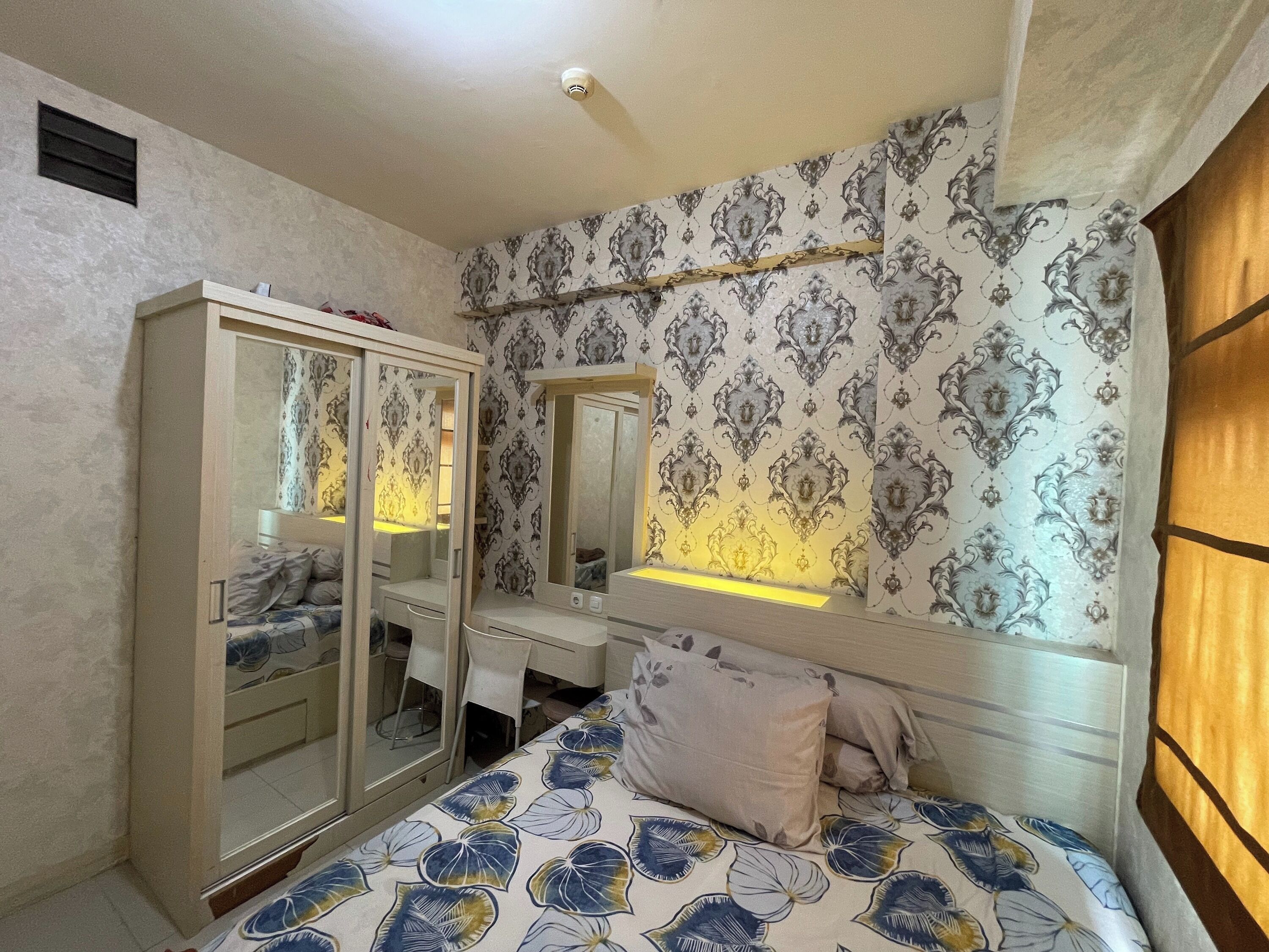 A bedroom with a bed, a wardrobe, a desk, and a mirror.