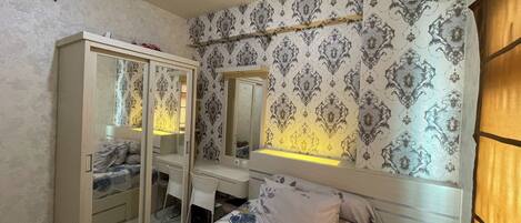 A bedroom with a bed, a wardrobe, a desk, and a mirror.