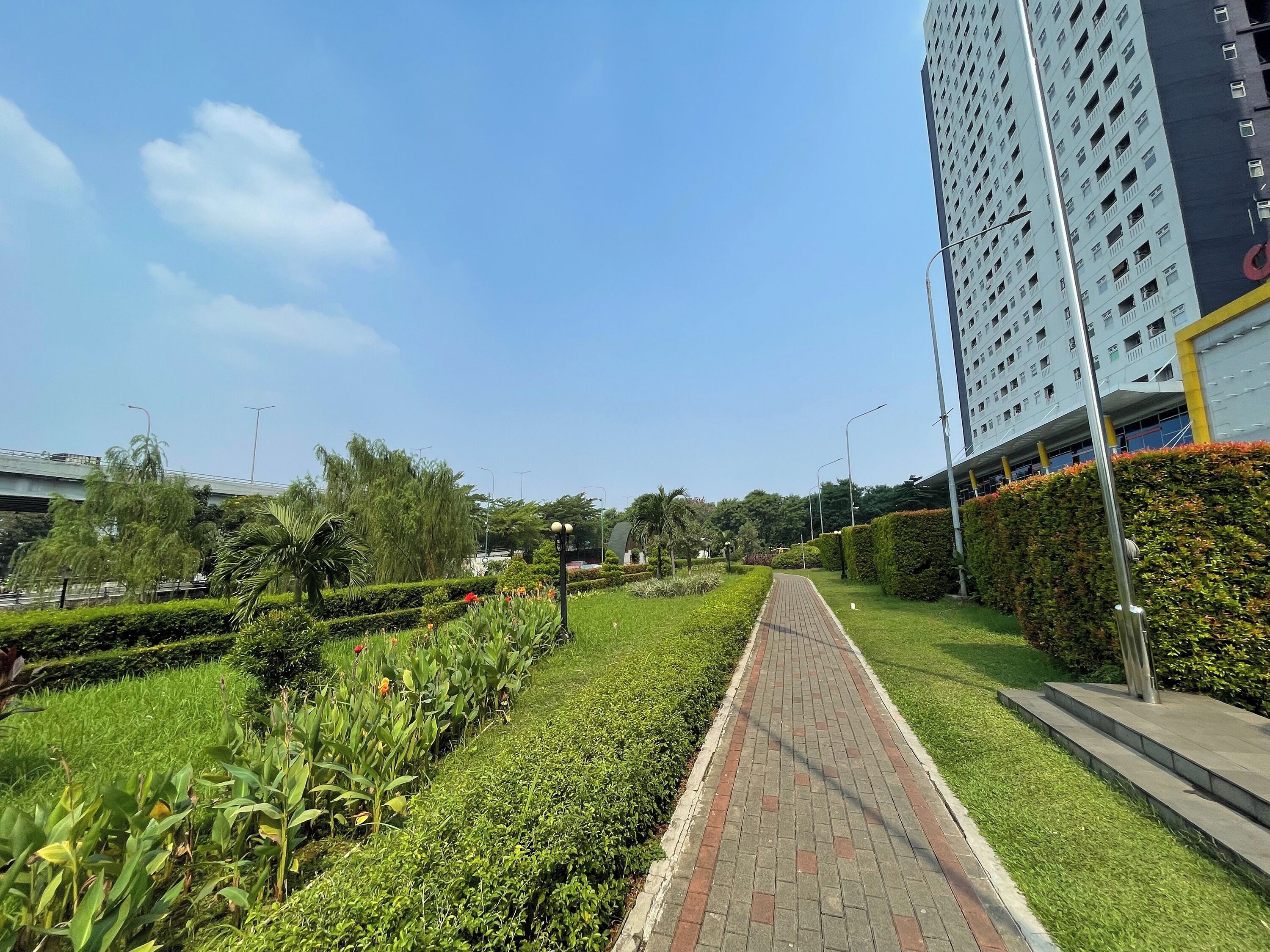A pathway lined with greenery and a tall building with a distinctive logo.