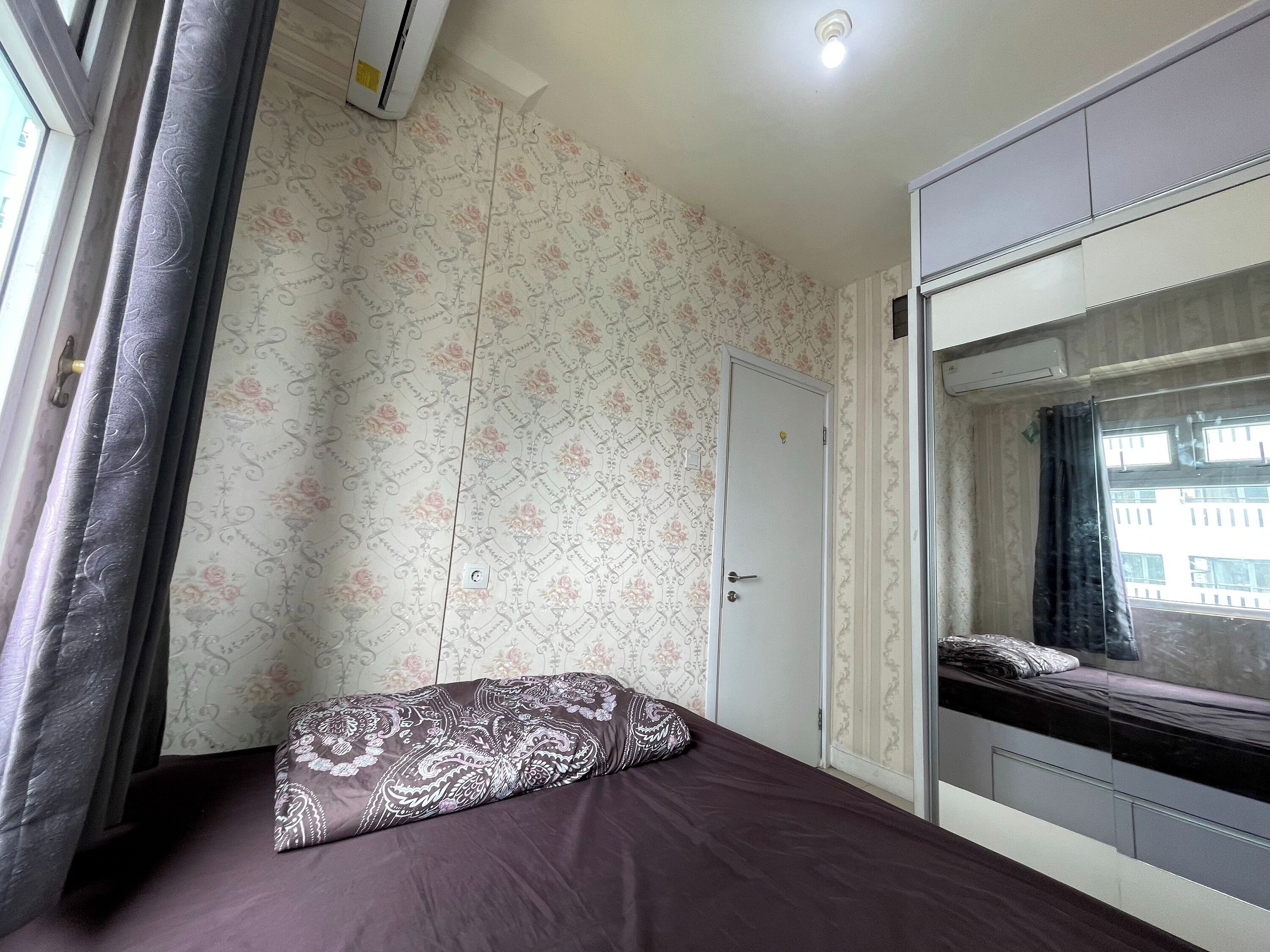 A bedroom with a bed, a wardrobe, and a window with curtains.