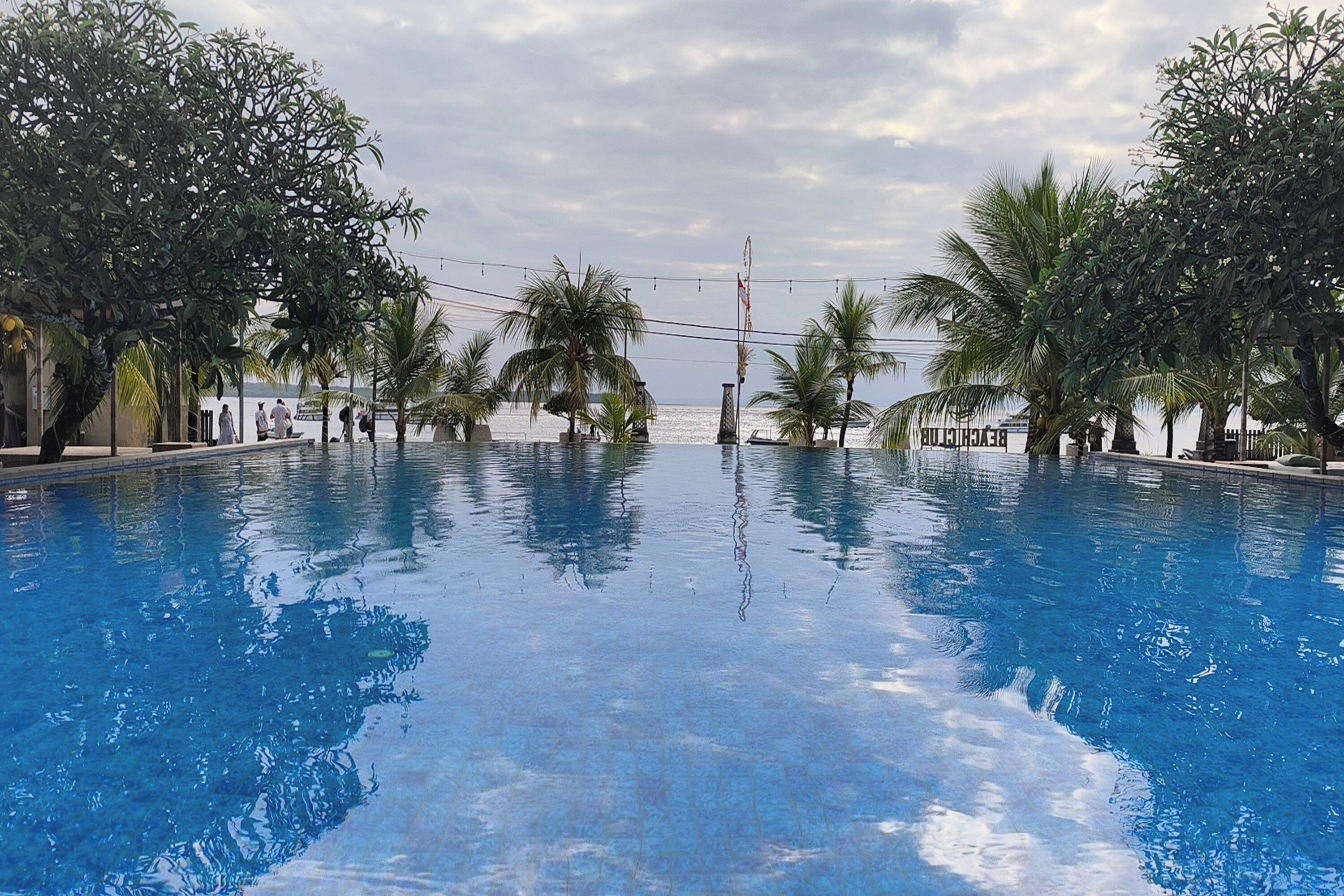 A swimming pool with clear blue water, surrounded by palm trees and a view of the sea.