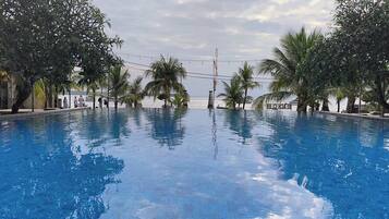 A swimming pool with clear blue water, surrounded by palm trees and a view of the sea.