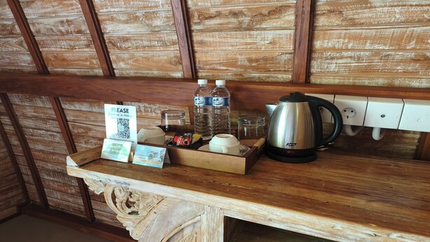 Una barra de madera con un cartel con un código QR, botellas de agua, un frasco de vidrio, una tetera y una bandeja con una taza y una caja.