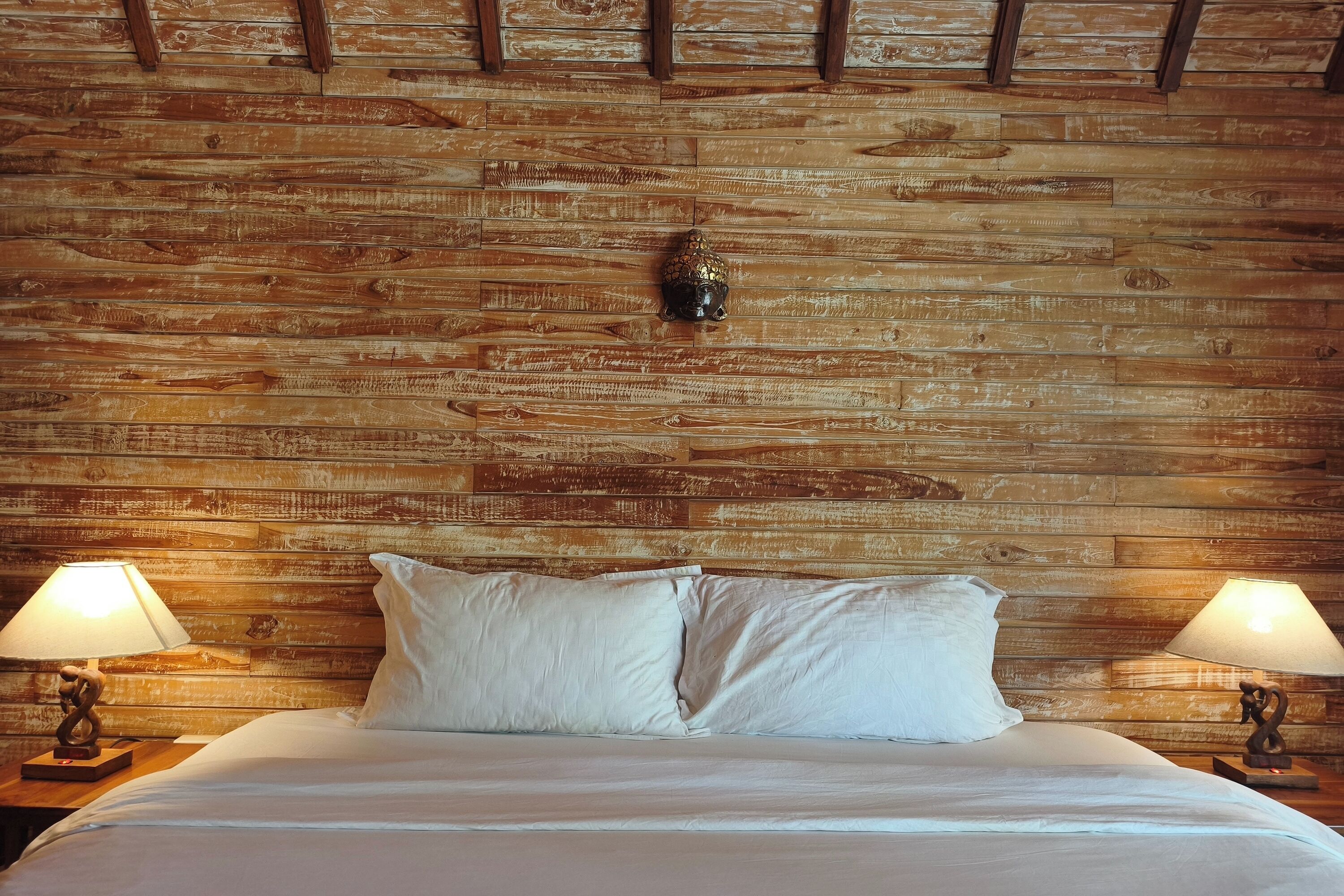 A bed with white bedding, two bedside lamps, and a wooden headboard with a decorative element.