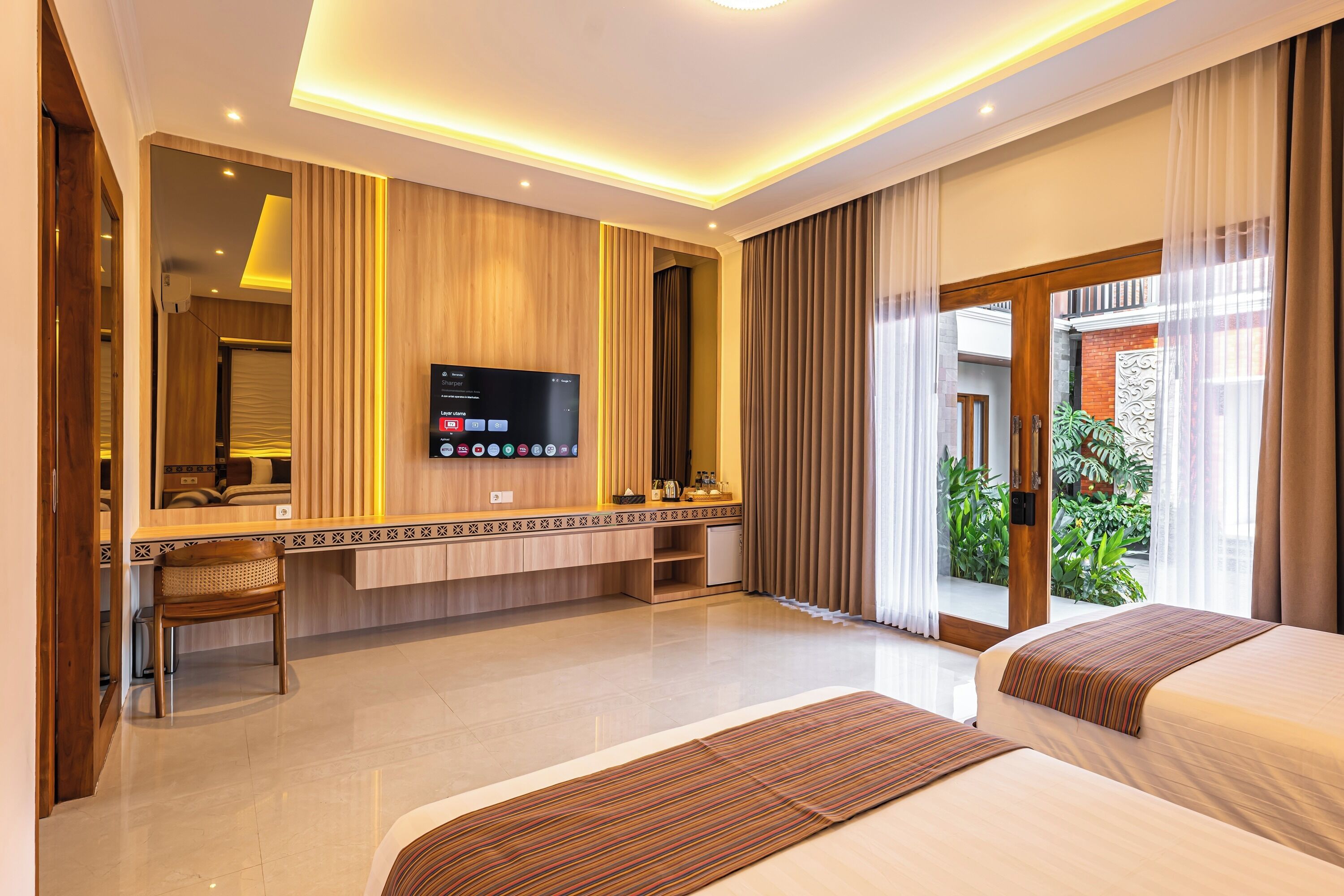 A hotel room with a bed, a desk, a television, and a view of greenery outside.