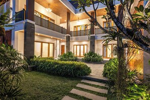 A multi-level residential building with a central courtyard, featuring a staircase, potted plants, and a well-lit entrance.