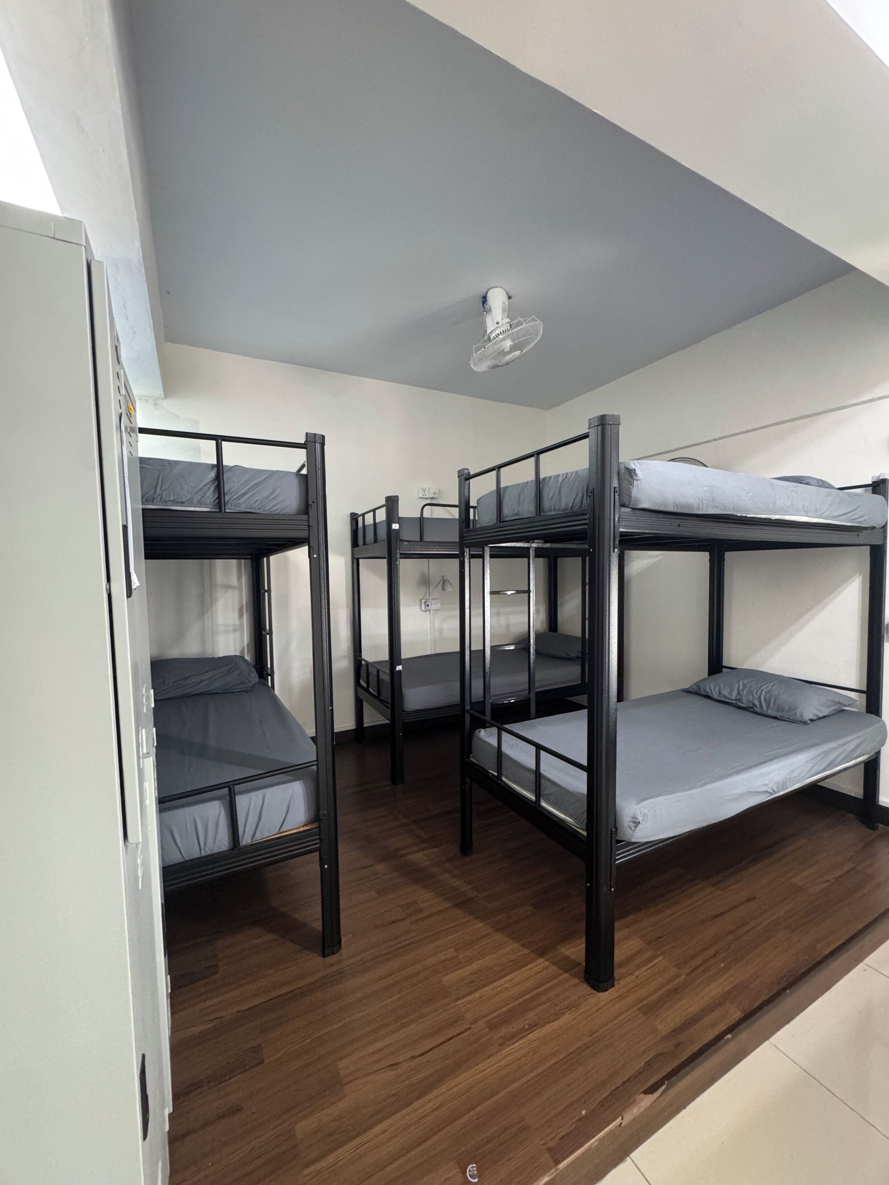 Quarto de dormitório com beliches, piso de madeira e ventoinha no teto.