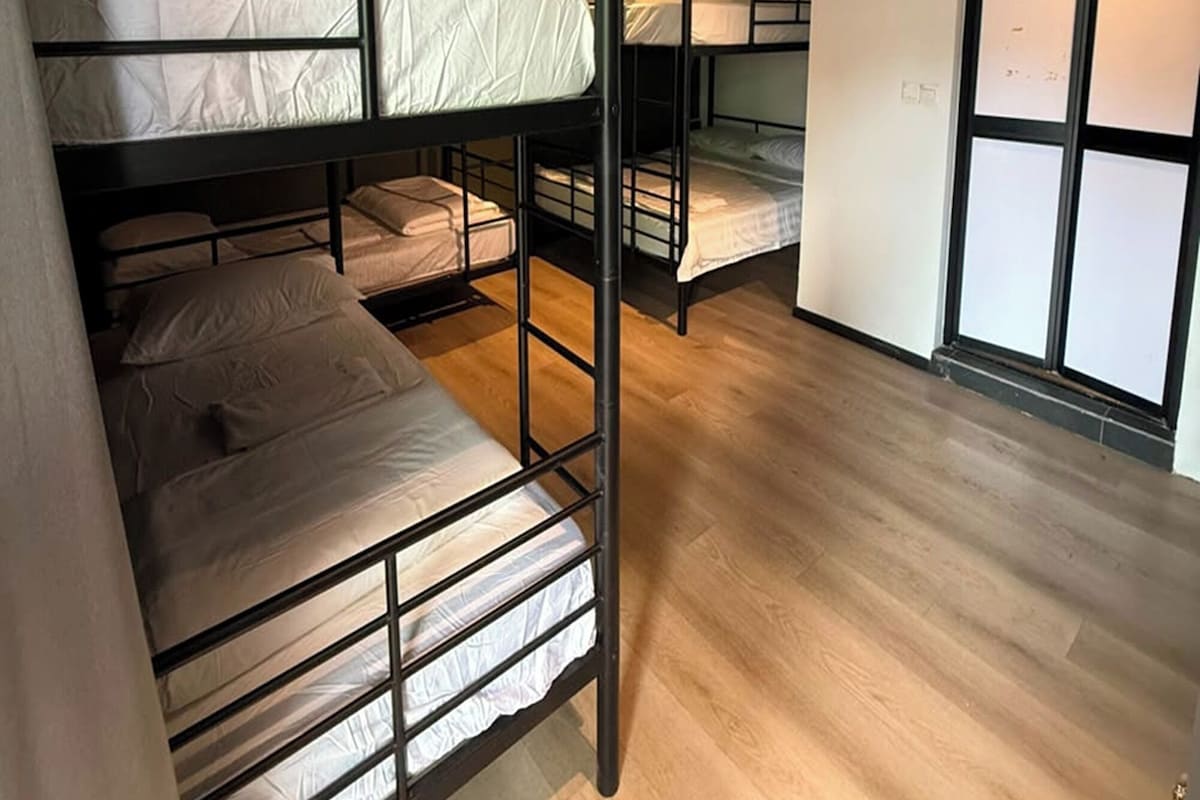 A dormitory room with bunk beds, wooden flooring, and an air conditioning unit.