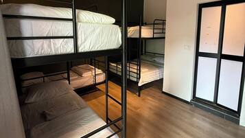 A dormitory room with bunk beds, wooden flooring, and an air conditioning unit.