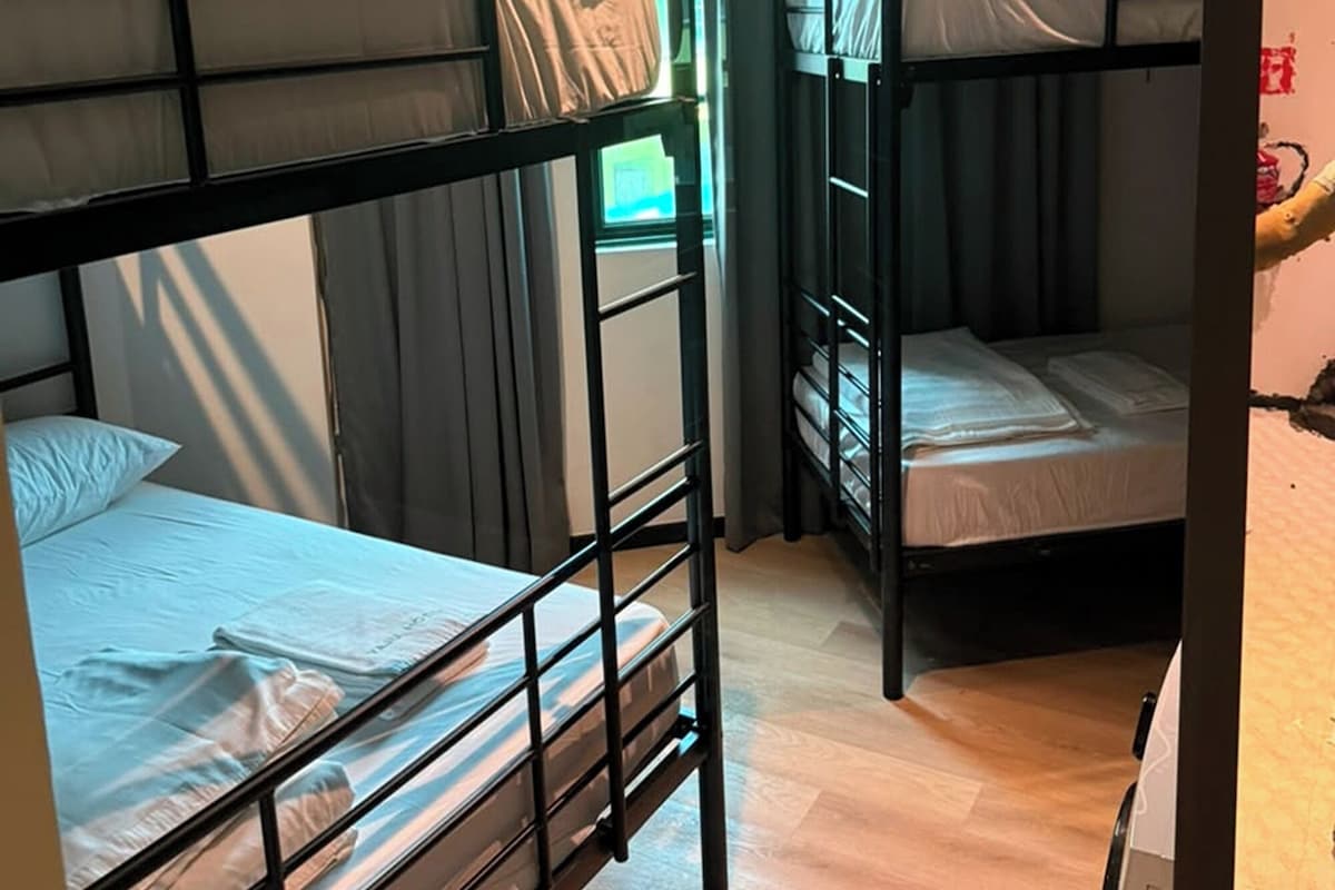 A dormitory room with bunk beds, a wooden floor, and a window with curtains.