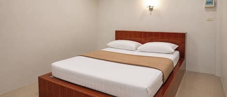 A single bed with a wooden headboard and a beige blanket, a wall-mounted light fixture, and a small picture frame on the wall.