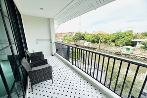 Uma varanda com guarda-corpo de metal preto, uma cadeira de vime e piso de azulejos.